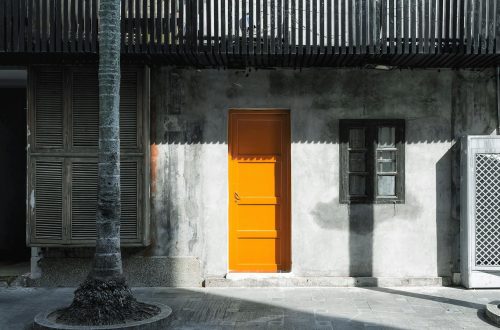 Vibrant orange door contrasts with a rustic concrete wall adorned with windows.