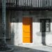 Vibrant orange door contrasts with a rustic concrete wall adorned with windows.