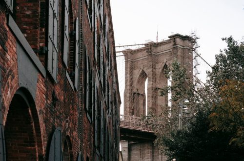 Classic view of the Brooklyn Bridge with historic urban architecture and foliage.