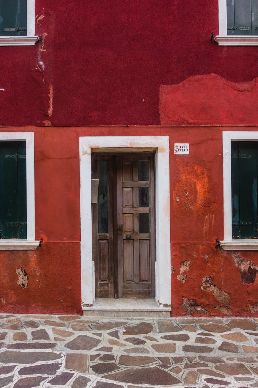 Vibrant red and orange facade of a Venetian house featuring a rustic wooden door and paved sidewalk.