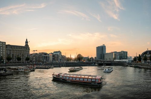Scenic view of Amsterdam canals at sunset with tour boats cruising and cityscape backdrop.