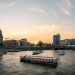 Scenic view of Amsterdam canals at sunset with tour boats cruising and cityscape backdrop.