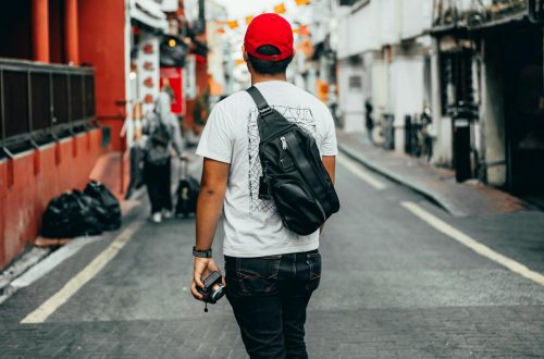 Young adult man exploring a colorful urban street with camera in hand, capturing lively surroundings.