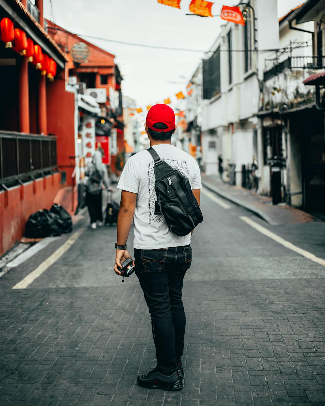 Young adult man exploring a colorful urban street with camera in hand, capturing lively surroundings.