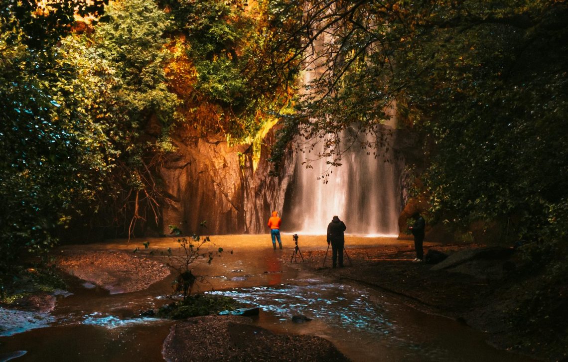 People photographing a scenic waterfall in the lush forests of Cerveteri, Italy.