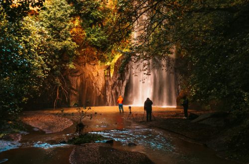 People photographing a scenic waterfall in the lush forests of Cerveteri, Italy.