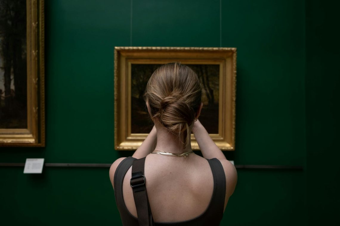 Back view of a woman photographing a painting in an art gallery.