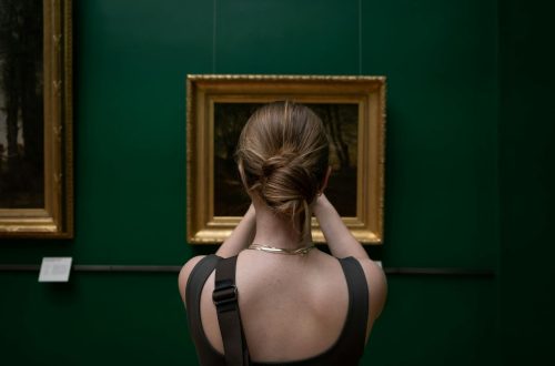 Back view of a woman photographing a painting in an art gallery.