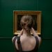 Back view of a woman photographing a painting in an art gallery.