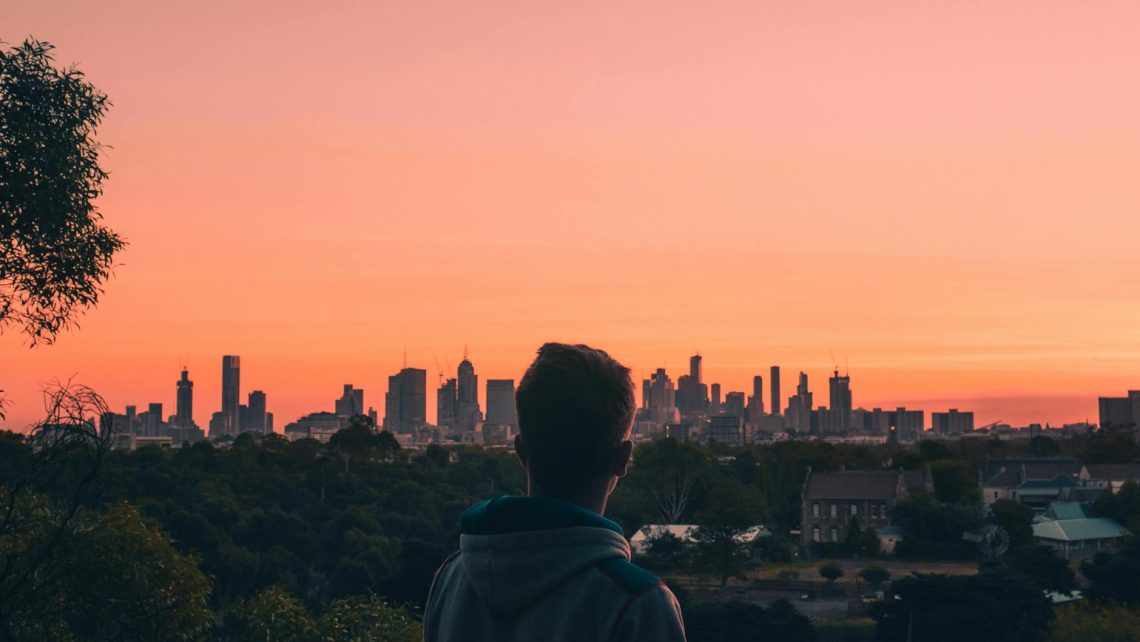 A person admires the Melbourne skyline at sunset, creating a stunning silhouette against a vibrant sky.