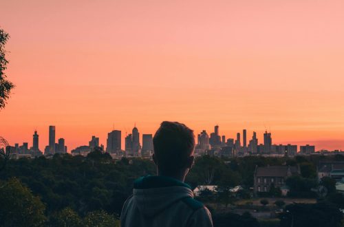 A person admires the Melbourne skyline at sunset, creating a stunning silhouette against a vibrant sky.