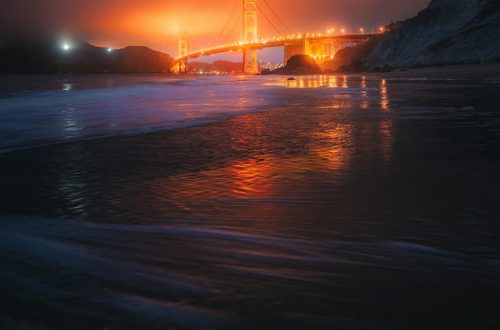 Iconic Golden Gate Bridge reflecting on ocean during a dramatic vibrant dusk in San Francisco.