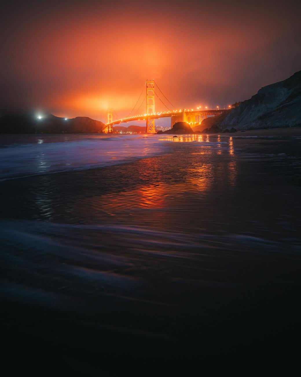 Iconic Golden Gate Bridge reflecting on ocean during a dramatic vibrant dusk in San Francisco.