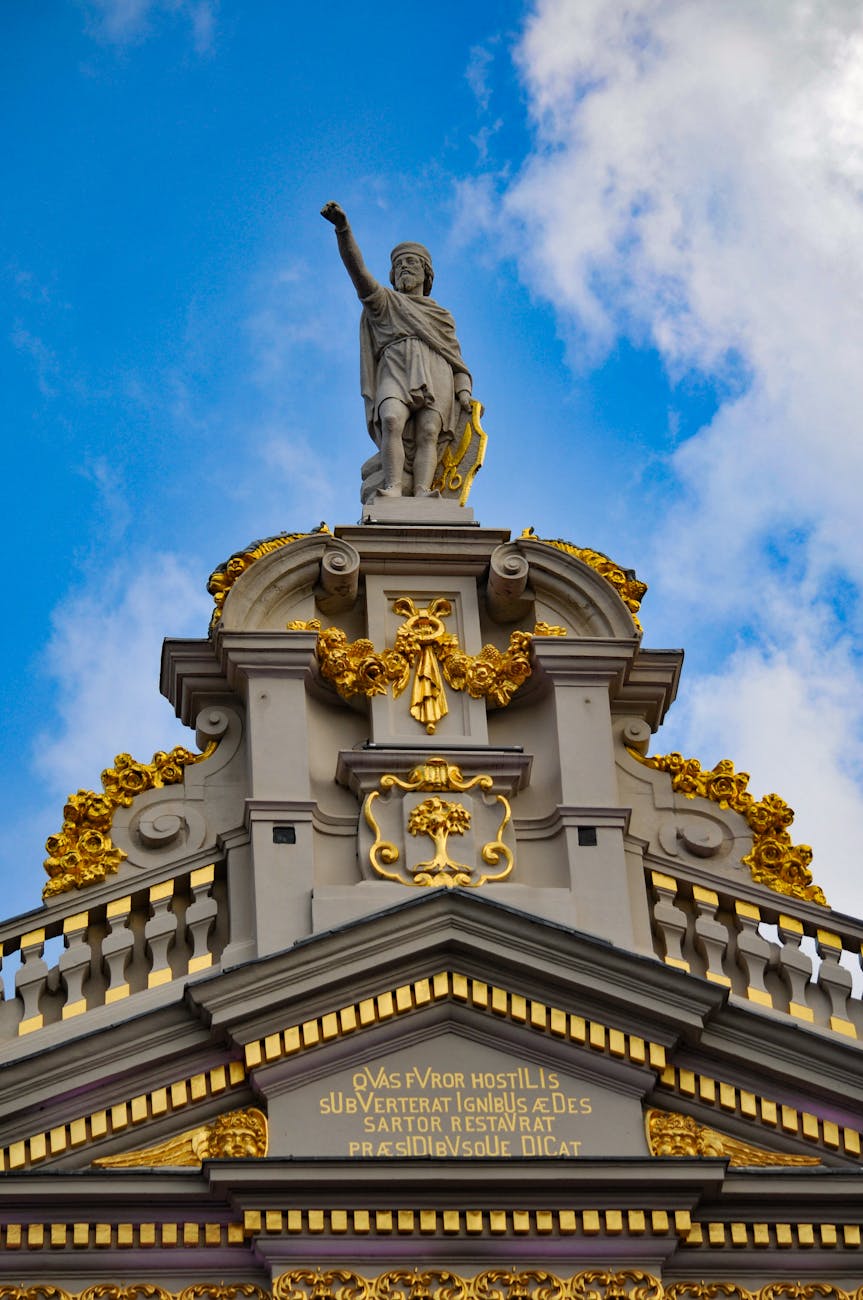 Ornate architectural detail with golden statue against a blue sky in Brussels, Belgium.