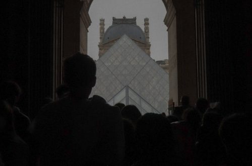 Silhouettes of people in front of the iconic Louvre Pyramid in Paris, France.