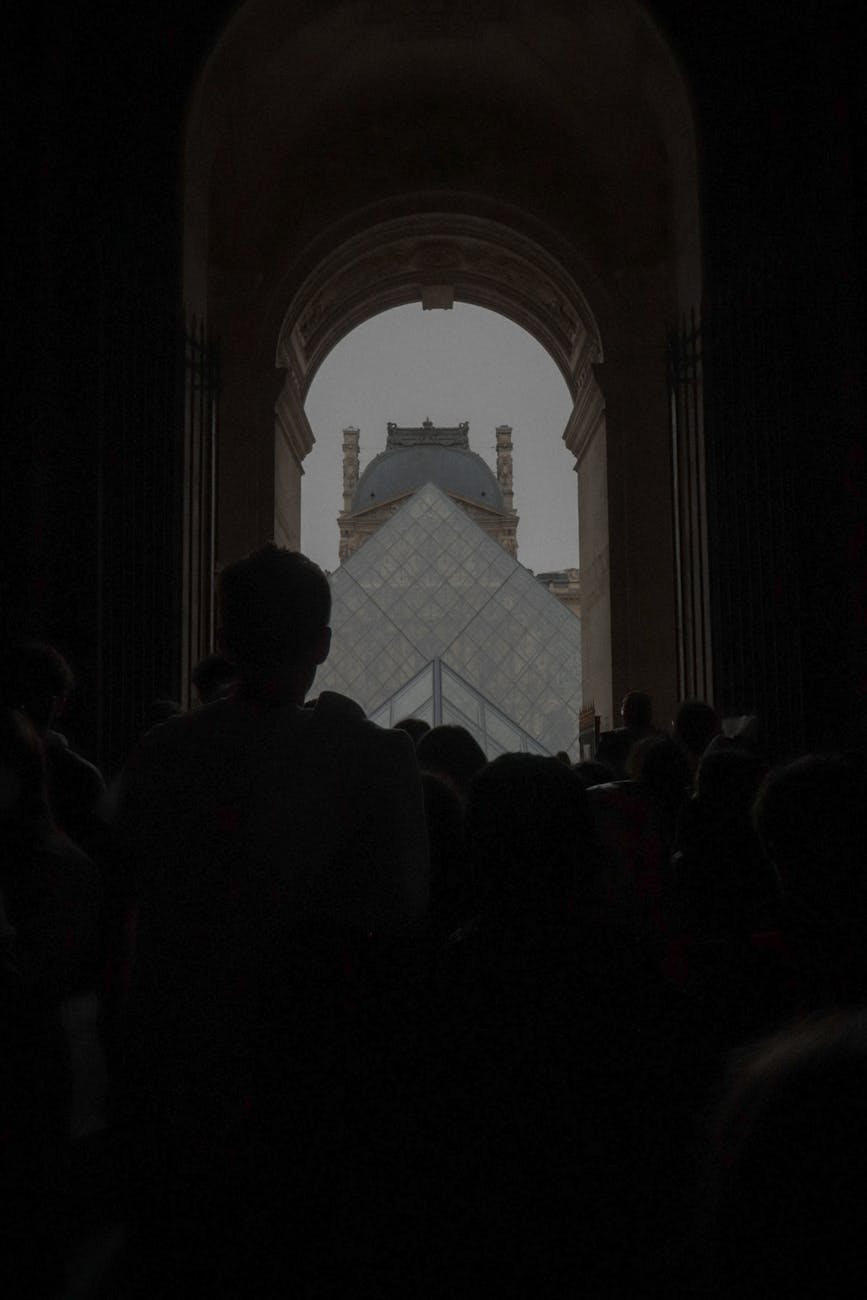 Silhouettes of people in front of the iconic Louvre Pyramid in Paris, France.