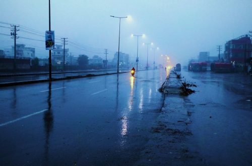 Rain-soaked street at twilight with glowing streetlights and misty atmosphere.