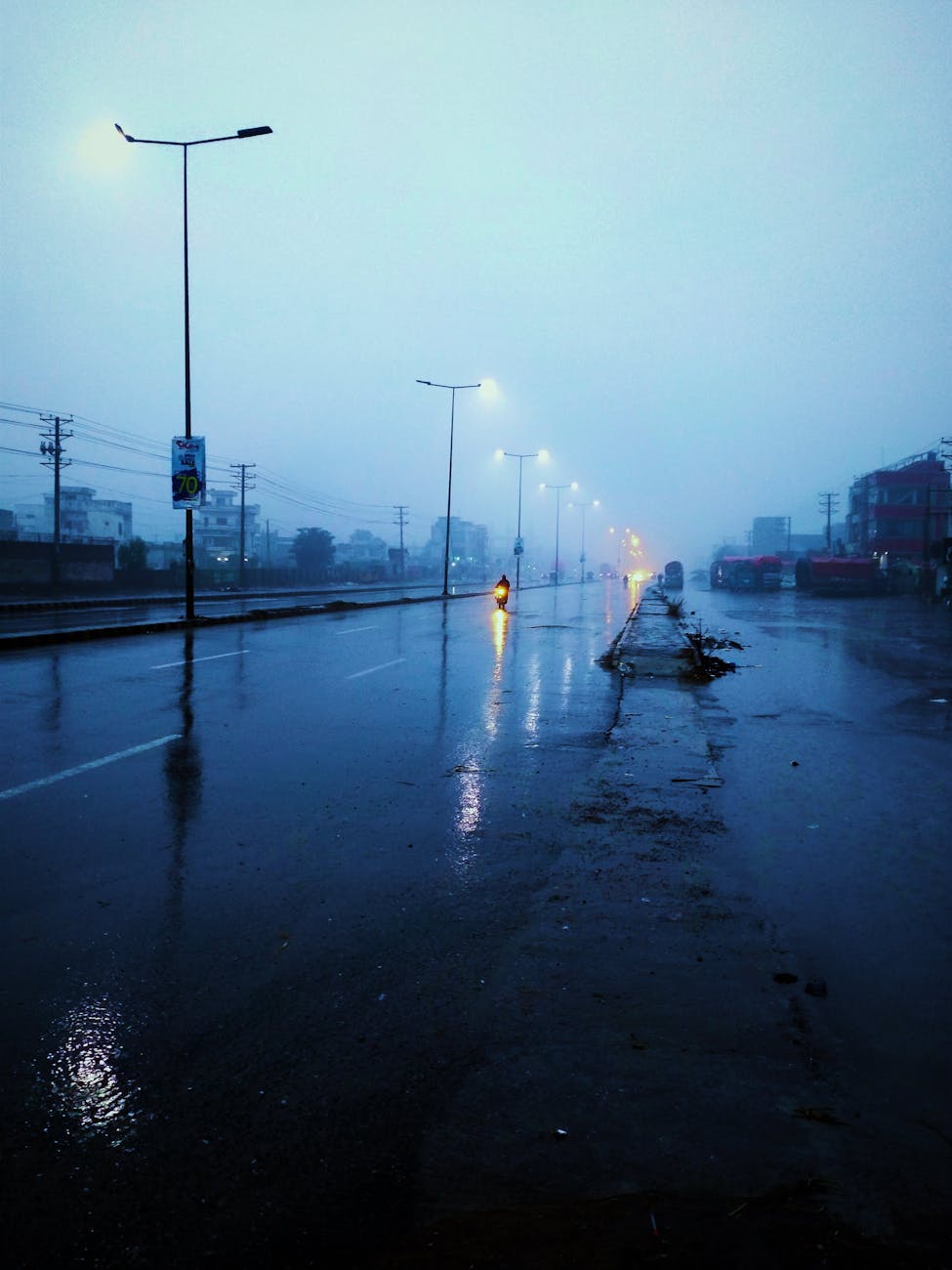 Rain-soaked street at twilight with glowing streetlights and misty atmosphere.
