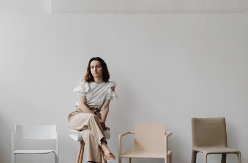 Woman sitting on a stool in a minimalist room with modern chairs.