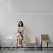 Woman sitting on a stool in a minimalist room with modern chairs.