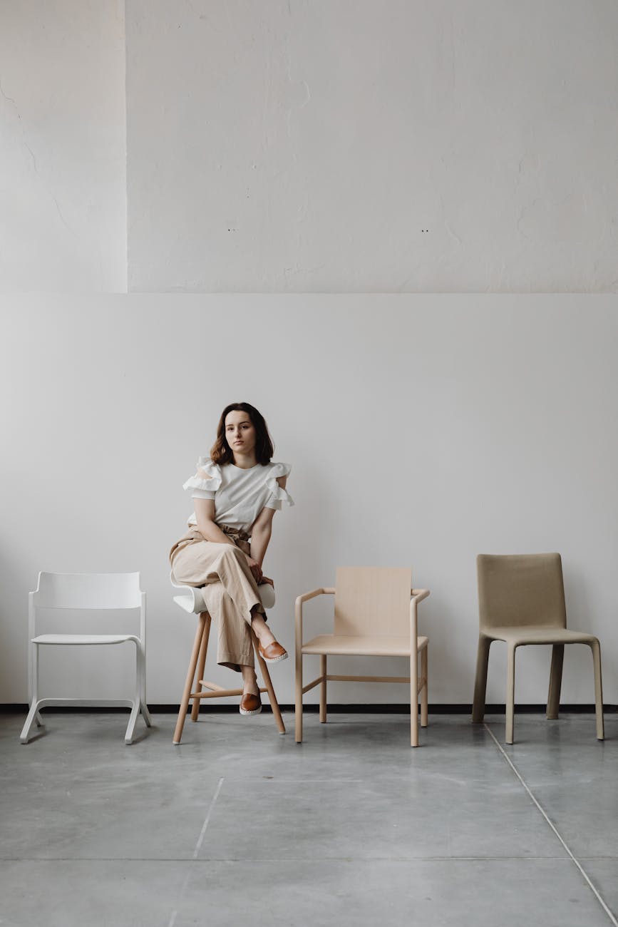Woman sitting on a stool in a minimalist room with modern chairs.
