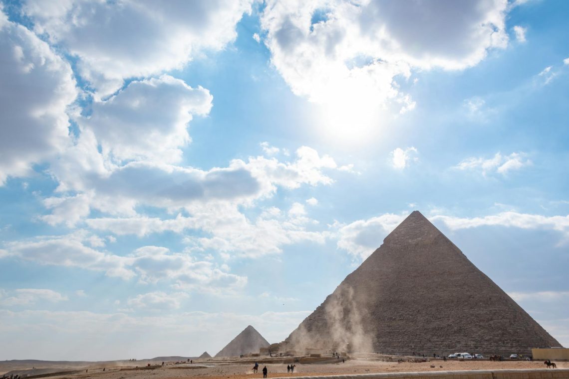 A stunning view of the Giza pyramids beneath a bright, cloud-dotted sky, perfect for travel enthusiasts.