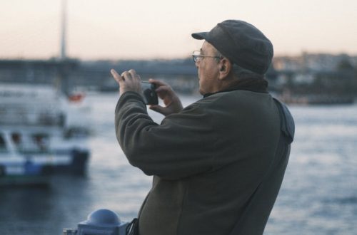 Older man using smartphone to capture scenic view of Istanbul waterfront during sunset.