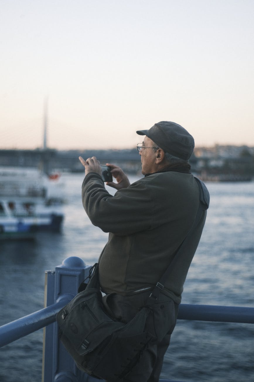 Older man using smartphone to capture scenic view of Istanbul waterfront during sunset.