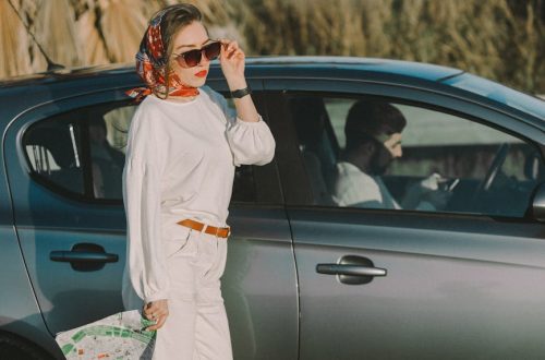 Stylish woman in sunglasses and scarf holding map beside parked car outdoors.