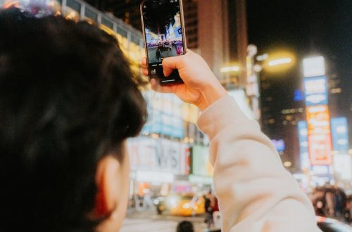 Tourist photographing vibrant city streets at night with a smartphone, capturing urban energy.