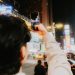 Tourist photographing vibrant city streets at night with a smartphone, capturing urban energy.