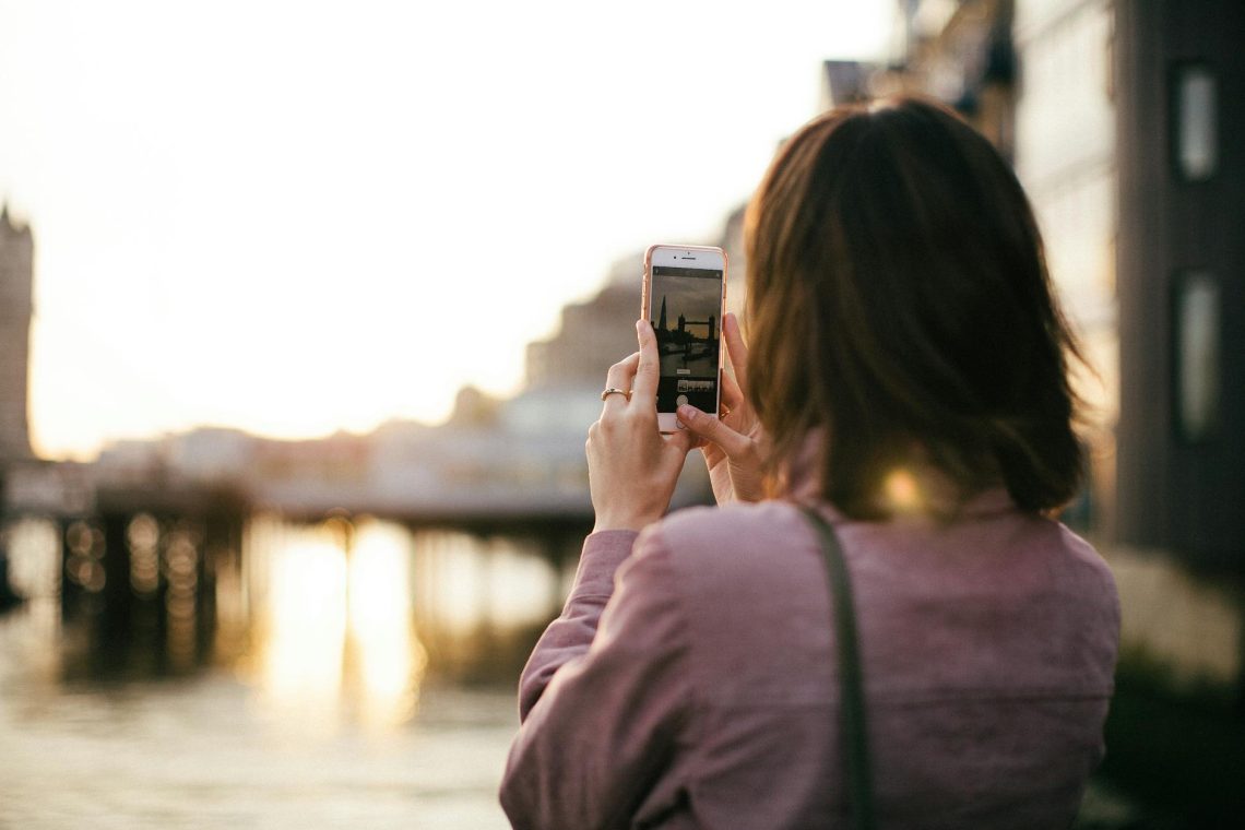 A woman takes a photo of London's skyline with her smartphone during a sunset stroll.