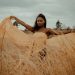 Graceful woman in flowing dress embraced by the golden wheat field under a cloudy sky.